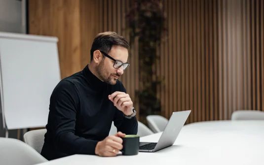 A Man Sitting At A Table With A Laptop And A Cup