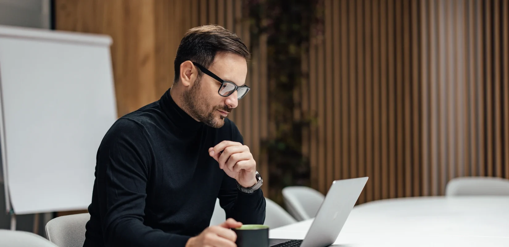 A Man Sitting At A Table With A Laptop And A Cup