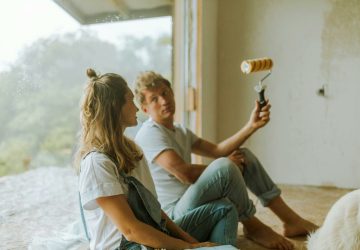 a man and woman sitting on the floor painting a wall