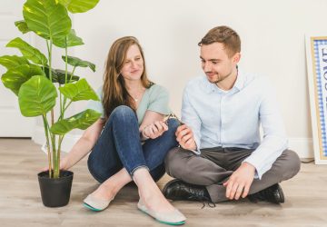 a man and woman sitting on the floor next to a plant